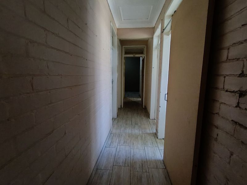A narrow interior hallway featuring tiled flooring and painted brick walls, providing access to multiple rooms within the property.