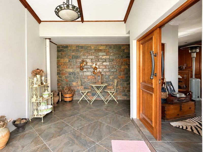Covered patio area featuring a rustic stone feature wall, tiled flooring, and a large timber entrance door leading into the home.