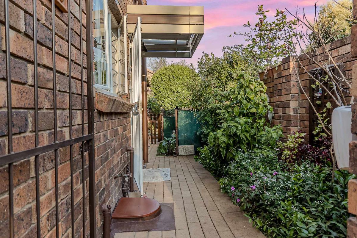 A side walkway featuring brick walls, paved flooring, and a secure metal gate entrance, leading to a landscaped garden area.