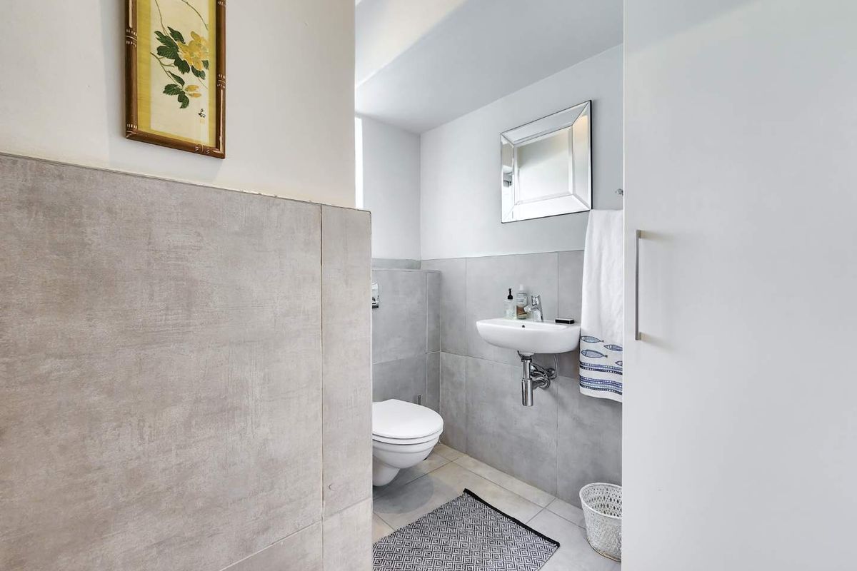 A modern, compact bathroom featuring a wall-mounted basin, wall-mounted toilet, and neutral large-format grey tiling throughout.