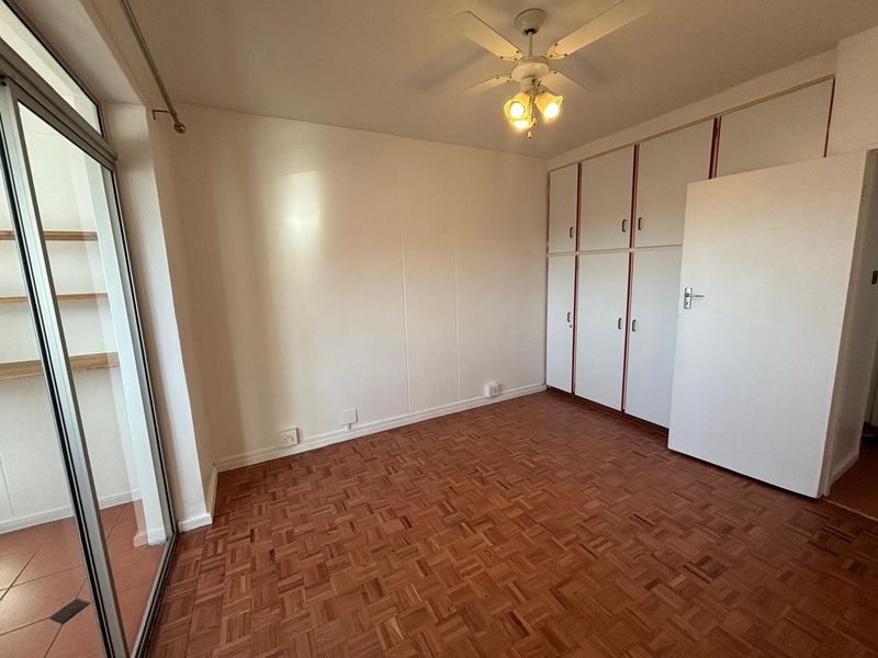 An empty bedroom featuring classic parquet flooring, built-in storage cupboards, a ceiling fan, and a sliding glass door leading to an outdoor area.