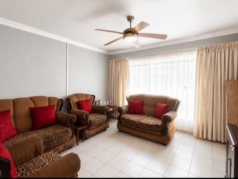 A well-lit living room featuring tiled flooring, crown molding, and a central ceiling fan, providing a comfortable and functional space.