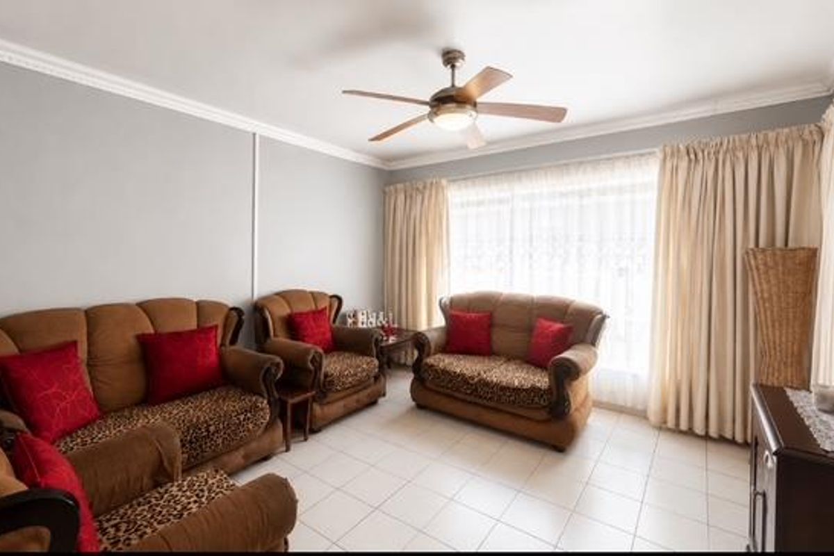 A well-lit living room featuring tiled flooring, crown molding, and a central ceiling fan, providing a comfortable and functional space.