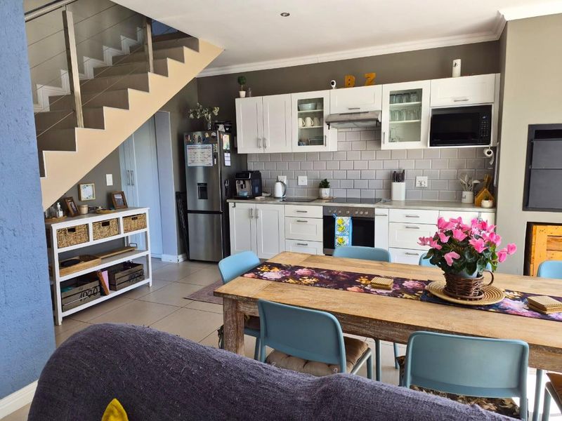 Open plan kitchen and dining area featuring white cabinetry, subway tile backsplash, integrated appliances, and a modern staircase with glass balustrade.