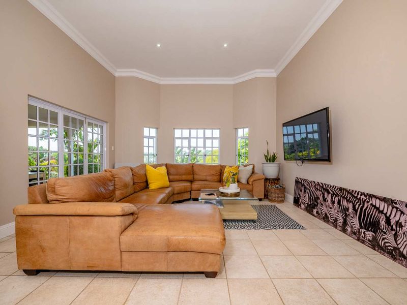 Spacious living room featuring neutral walls, tiled flooring, crown molding, and large windows providing ample natural light and garden views.