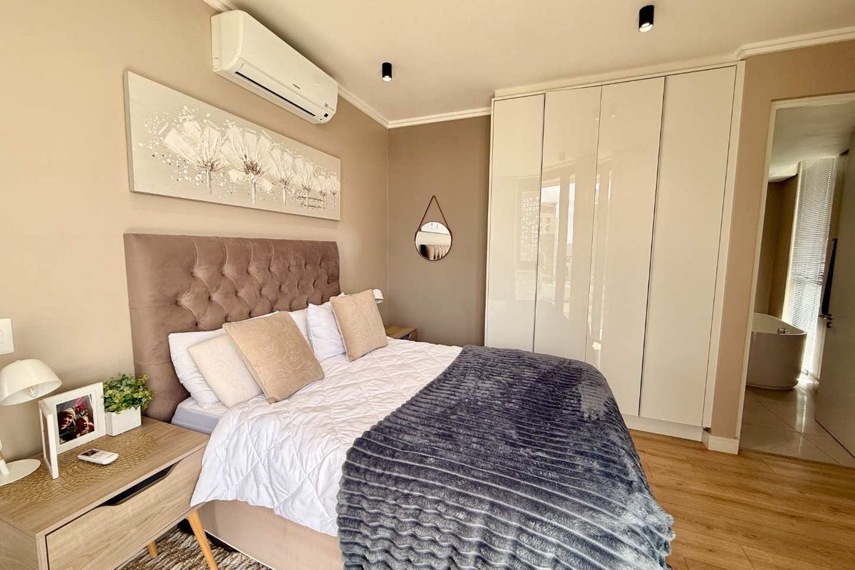 A well-maintained bedroom featuring built-in high-gloss wardrobes, modern recessed ceiling lighting, and a wall-mounted air conditioning unit.