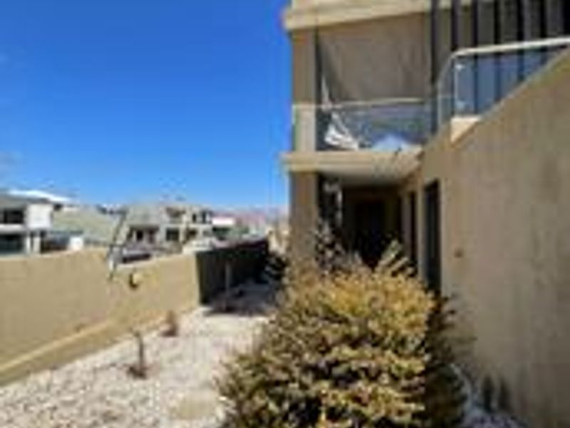 Rear exterior view of the property featuring a gravel garden, retaining wall, and an upper-level balcony with a glass balustrade.