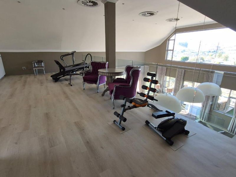 Spacious open-plan mezzanine area featuring light laminate flooring, extensive built-in cabinetry, a glass balustrade, and large windows providing ample natural light.