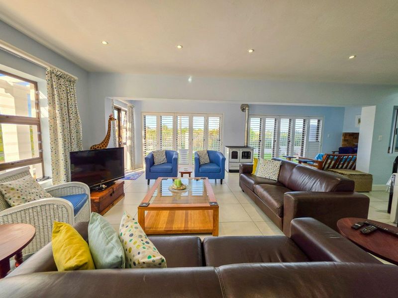 Spacious living room featuring tiled floors, recessed lighting, and a freestanding wood-burning stove, with large plantation shutters opening to the outdoors.