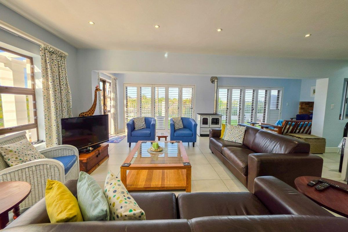 Spacious living room featuring tiled floors, recessed lighting, and a freestanding wood-burning stove, with large plantation shutters opening to the outdoors.