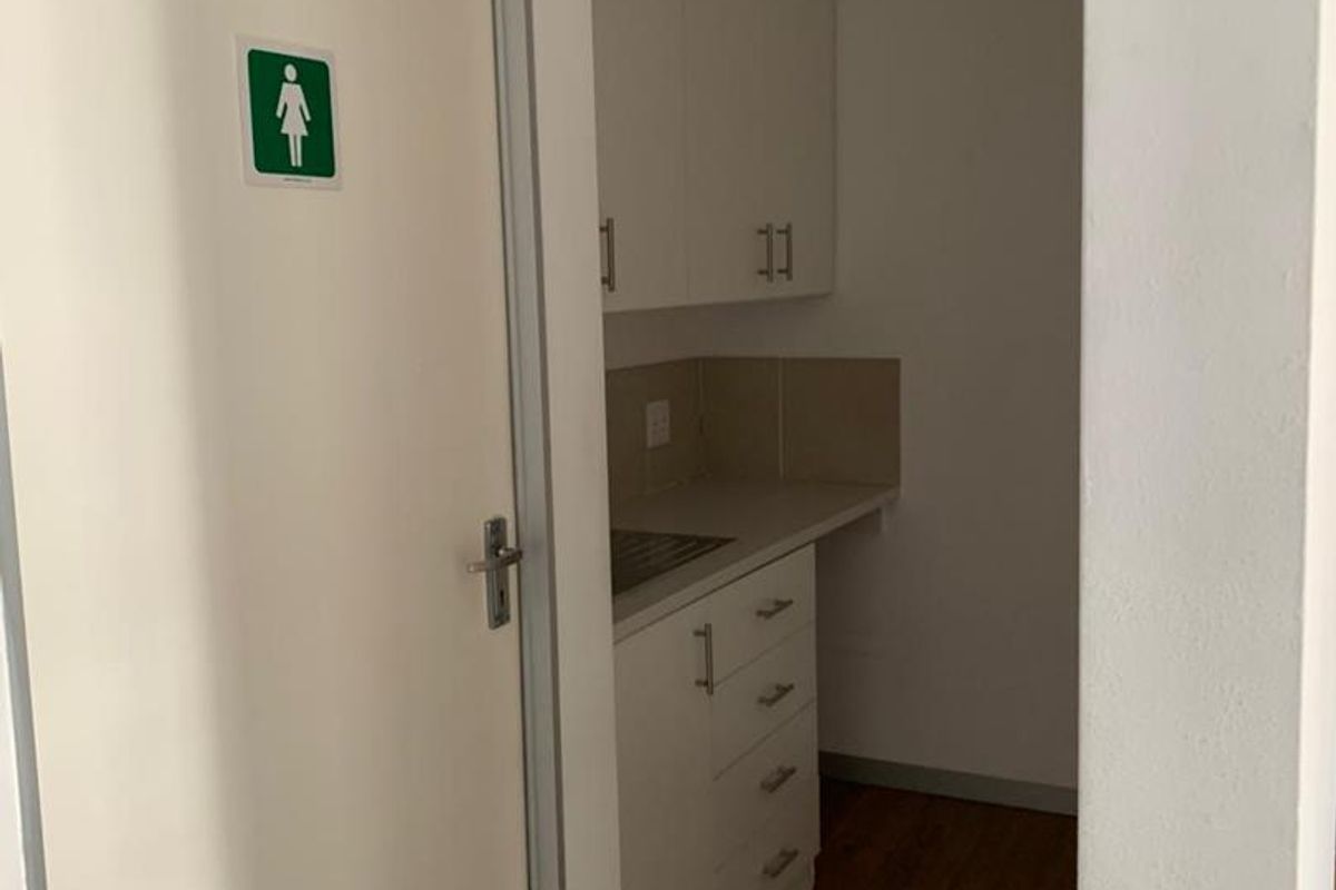 A compact kitchenette area featuring white cabinetry, a sink, and wood-look flooring, located adjacent to a restroom facility.