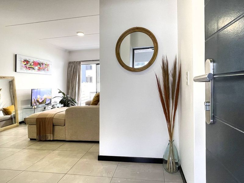 An inviting apartment entrance area featuring neutral tiled flooring, clean white walls, and a seamless transition into the open-plan living space.