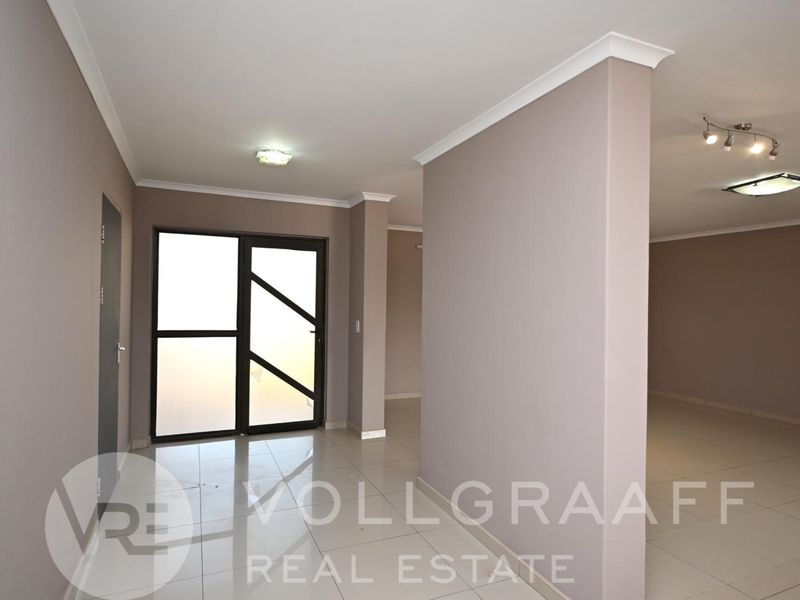 A bright and spacious entrance hall featuring neutral wall tones, polished tiled flooring, and modern recessed lighting, leading into an open-plan living area.