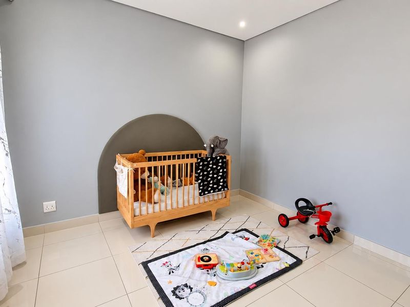 A bright and neutral bedroom featuring tiled flooring, recessed downlighting, and a clean, modern aesthetic suitable for a nursery or guest room.