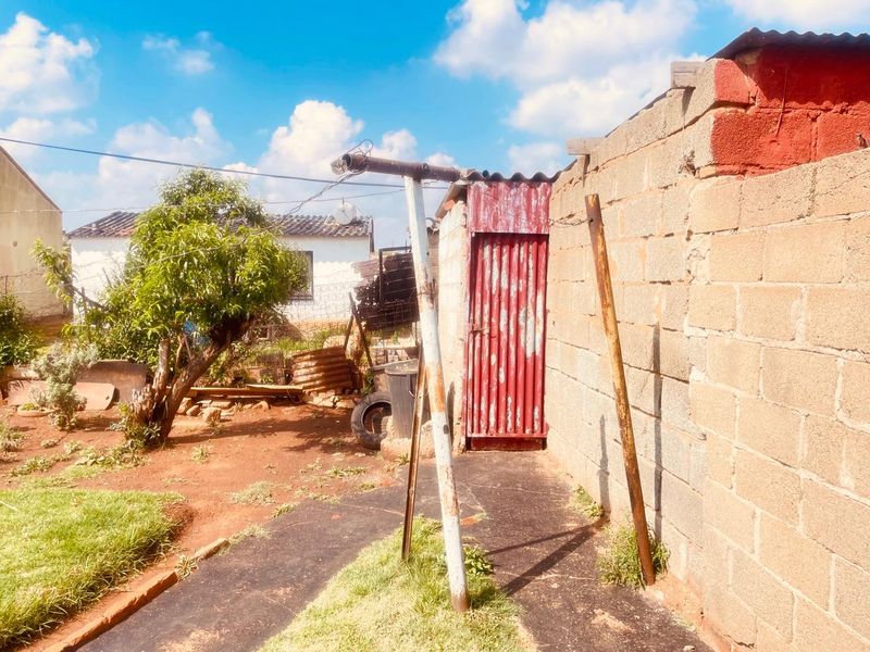 Rear exterior area featuring a cinder block boundary wall, a corrugated metal door, and a concrete pathway with weathered metal support structures.
