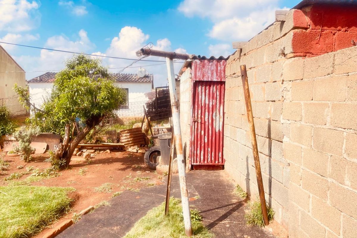 Rear exterior area featuring a cinder block boundary wall, a corrugated metal door, and a concrete pathway with weathered metal support structures.