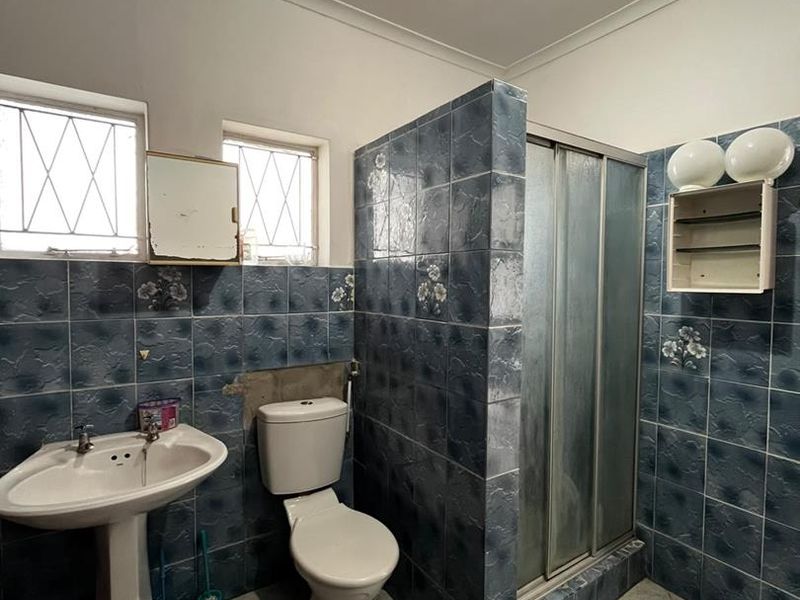 A dated bathroom featuring a pedestal basin, toilet, and shower enclosure with blue tiled walls and flooring, requiring cosmetic updates and repairs.