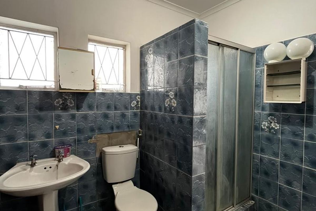 A dated bathroom featuring a pedestal basin, toilet, and shower enclosure with blue tiled walls and flooring, requiring cosmetic updates and repairs.