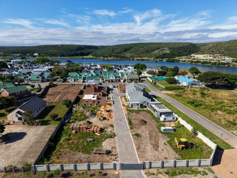 Aerial view of a residential development site featuring a paved driveway, perimeter wall, and ongoing construction work in a coastal estate setting.