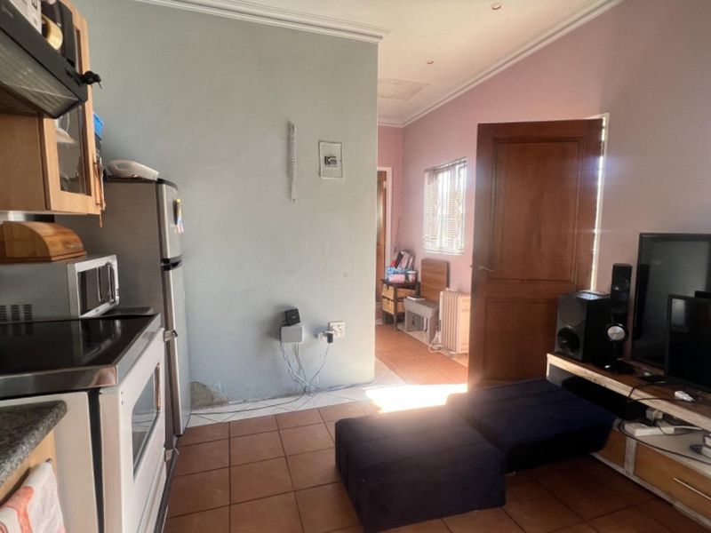 Open plan living area featuring tiled flooring, a compact kitchen with built-in stove and extractor fan, and access to an adjacent room.