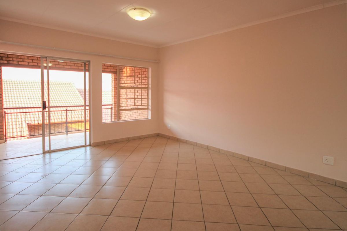 A bright, empty living area featuring neutral tiled flooring, large windows, and a sliding glass door leading to an outdoor balcony.