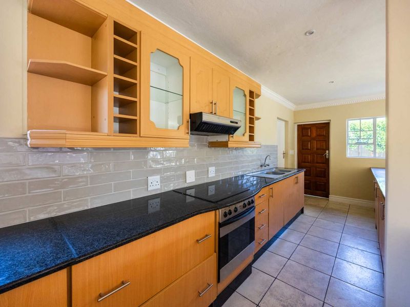 A functional kitchen featuring light wood cabinetry, dark granite countertops, a built-in stove with extractor fan, and neutral tiled flooring.