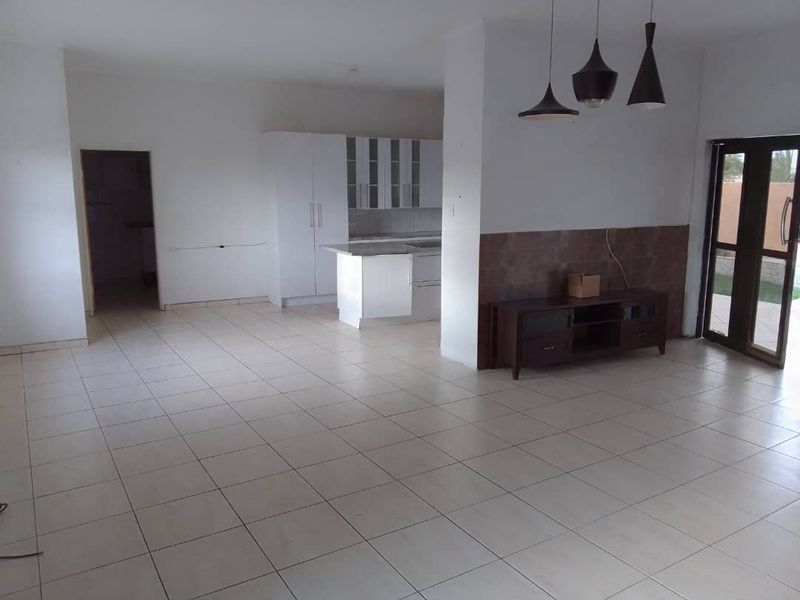 Spacious open-plan living area featuring tiled floors, a modern kitchen with built-in cabinetry, and direct access to the outdoors through glass doors.