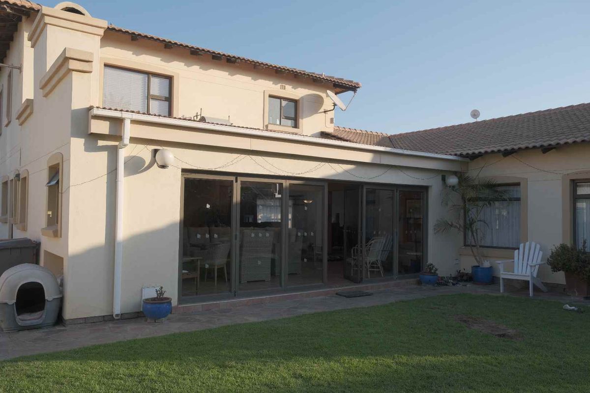 Rear view of the house featuring a paved patio area, large sliding glass doors, and a well-maintained lawn.