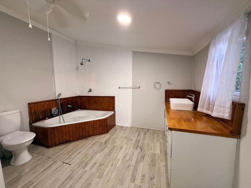 Spacious bathroom featuring a corner bathtub with wood paneling, a vessel sink on a wooden vanity, and light wood-look flooring.