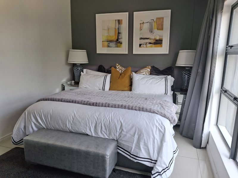 A well-maintained bedroom featuring tiled flooring, a large window for natural light, and a dark grey accent wall.