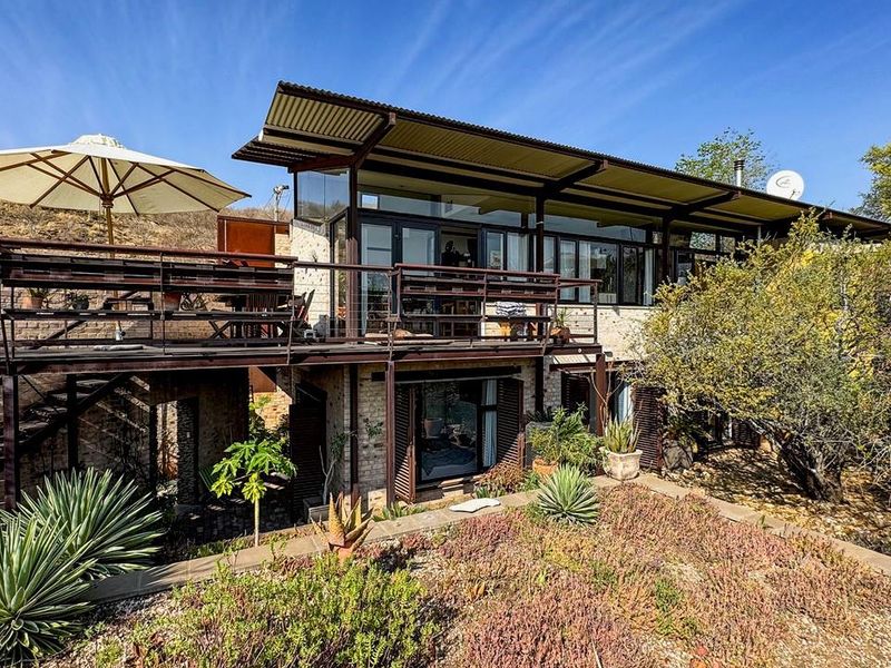 Rear view of a modern house featuring an elevated timber deck, corrugated metal roofing, and large sliding glass doors overlooking a landscaped garden.