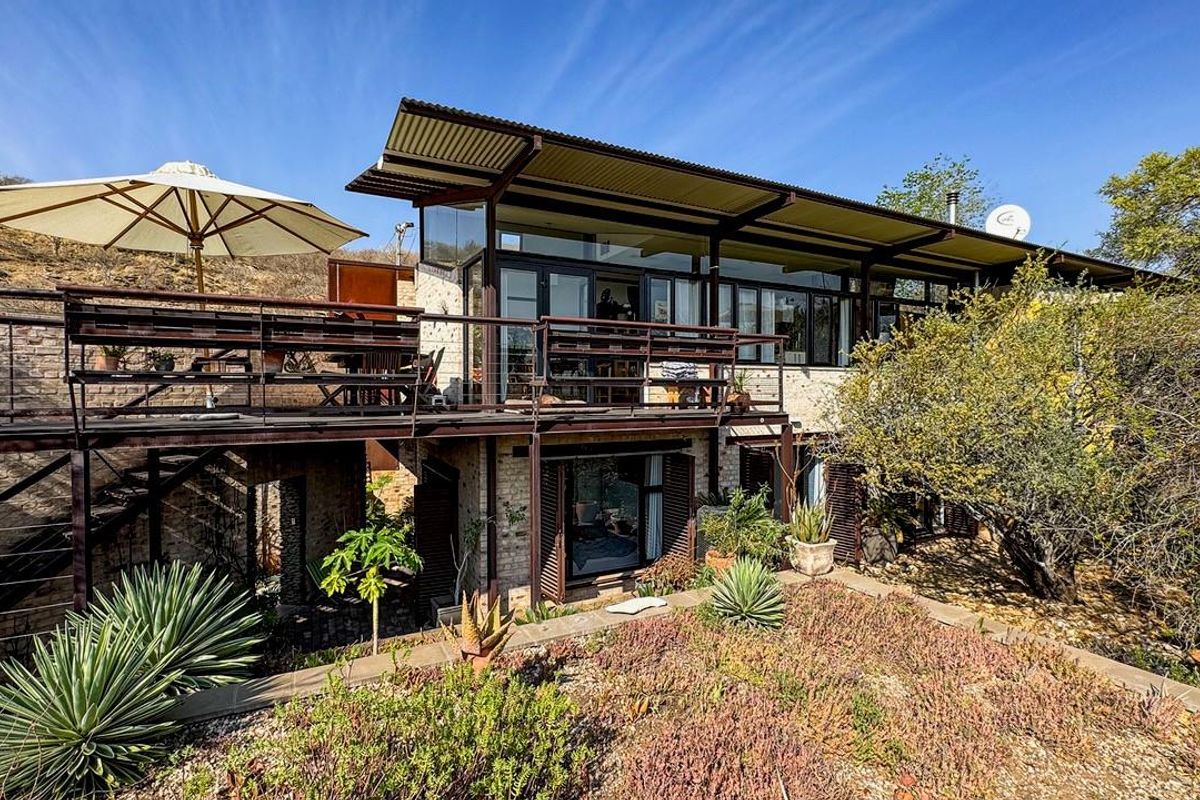 Rear view of a modern house featuring an elevated timber deck, corrugated metal roofing, and large sliding glass doors overlooking a landscaped garden.