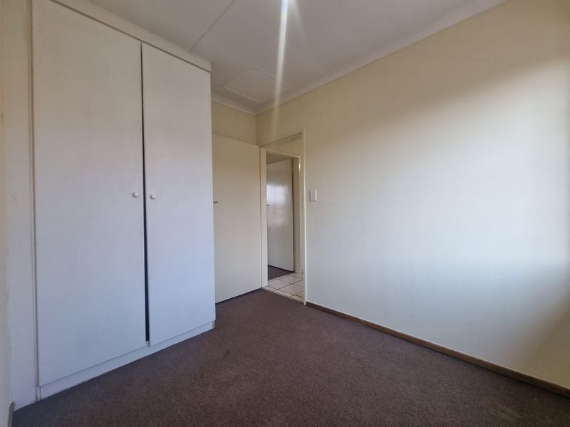 An empty bedroom featuring neutral walls, carpet flooring, and a built-in wardrobe, offering a blank canvas for personalization.