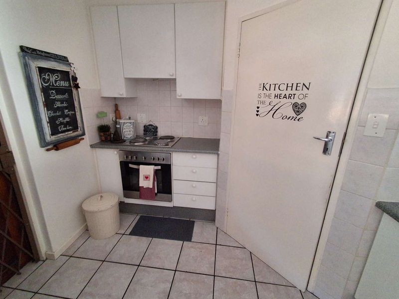 Compact kitchen featuring white cabinetry, built-in oven and hob, tiled backsplash, and tiled flooring.