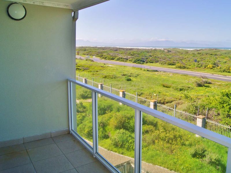 A balcony featuring a glass balustrade and tiled flooring, offering an expansive view of the surrounding coastal landscape and road.
