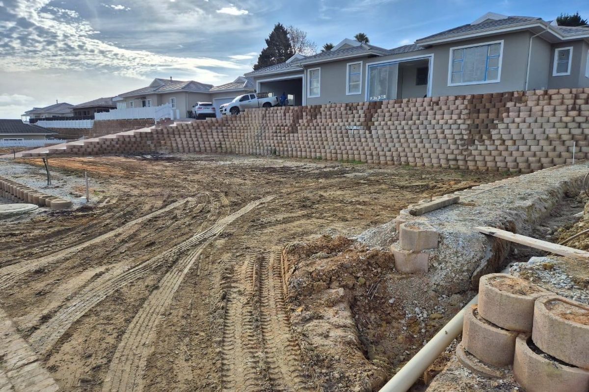 A view of a residential plot under development, featuring extensive retaining wall infrastructure and cleared, unlandscaped ground.