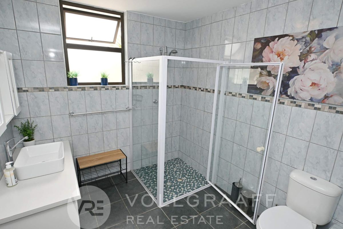 A functional bathroom featuring a glass-enclosed shower, modern vessel sink vanity, and tiled walls with a decorative mosaic border.