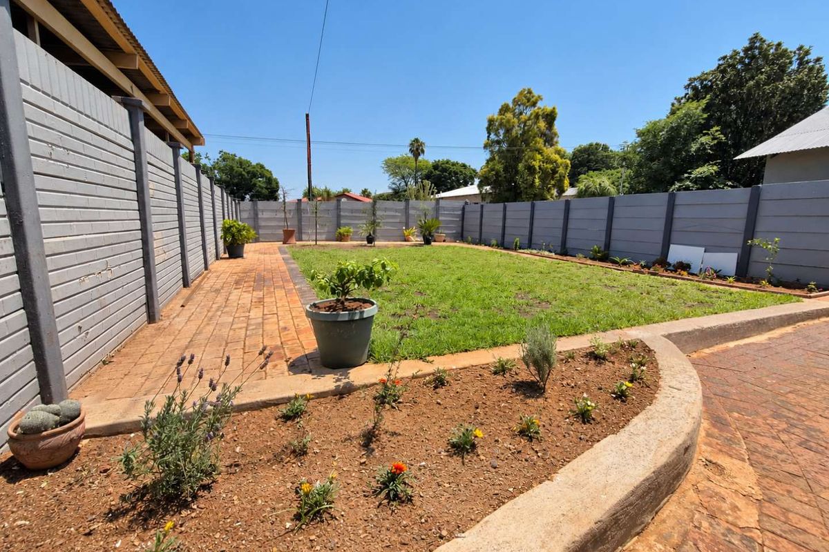 A well-maintained rear garden featuring a brick-paved patio, a curved concrete garden bed, and a secure precast concrete boundary wall.