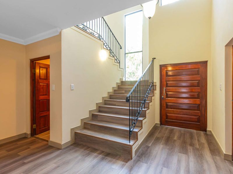 Spacious double-volume entrance hall featuring a grand staircase with wrought iron balustrades, wood-look laminate flooring, and a solid timber front door.