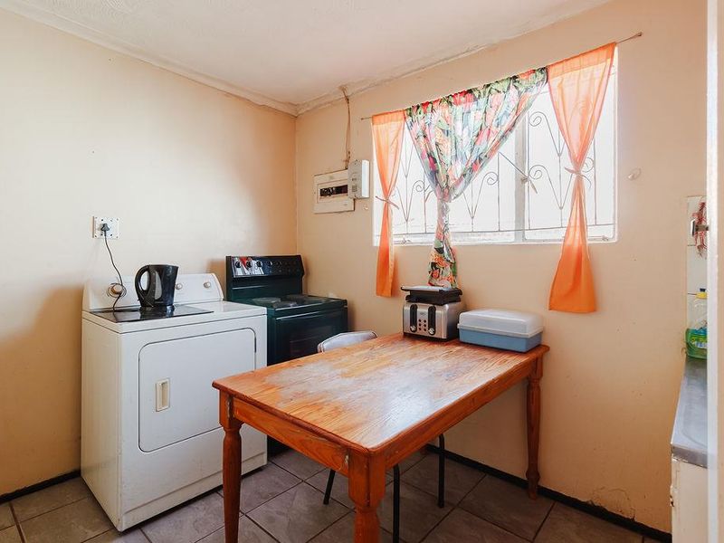 A functional kitchen area featuring tiled flooring, an electric stove, and a window with security bars, requiring cosmetic updates to improve its overall condition.