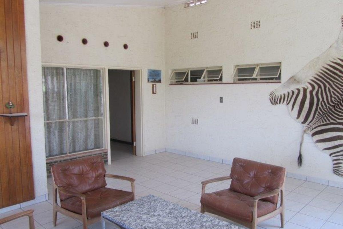 A spacious living area featuring tiled flooring, high ceilings with ventilation ports, and large windows allowing natural light into the room.