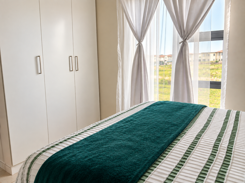 A bright bedroom featuring modern white built-in cupboards and a large window with natural light, overlooking a green landscape.