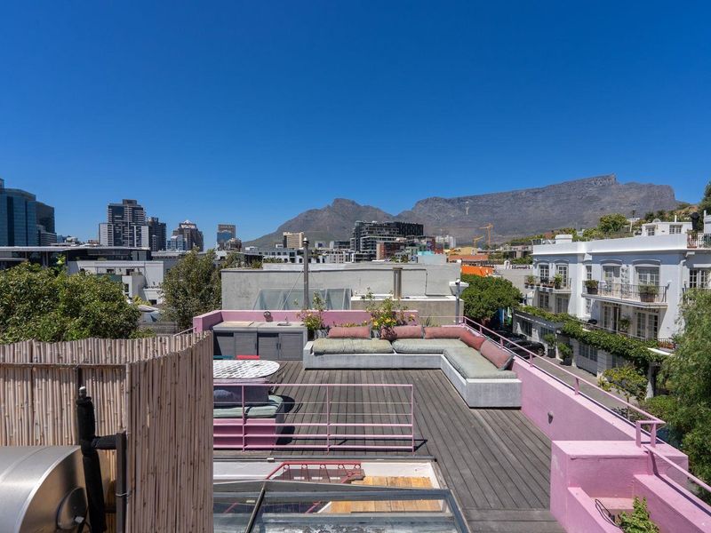 Spacious rooftop terrace featuring timber decking, built-in concrete seating, and an outdoor sink, offering panoramic city and mountain views.