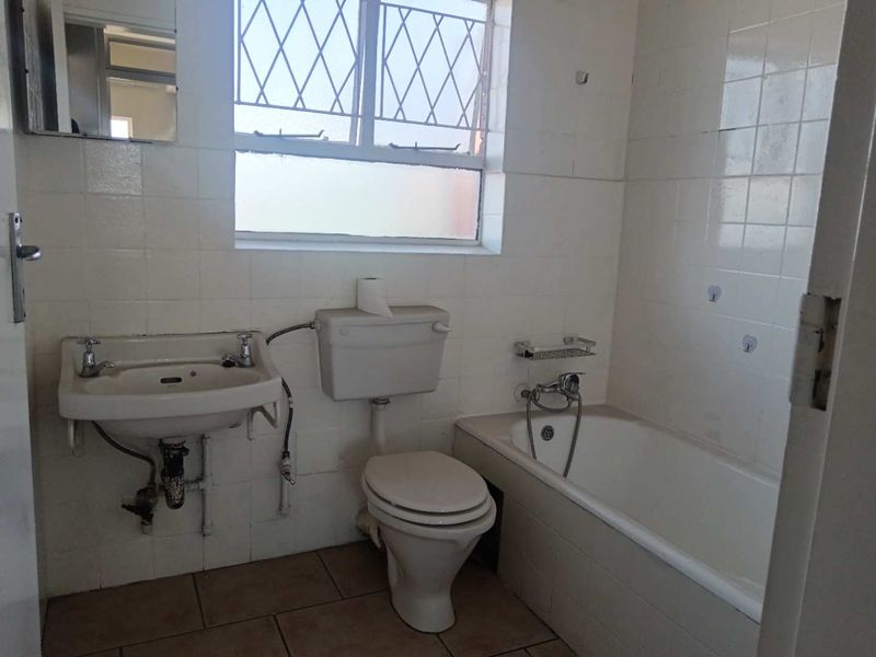 A dated bathroom featuring a wall-mounted basin, standard toilet, and bathtub with handheld shower mixer, finished with tiled walls and flooring.