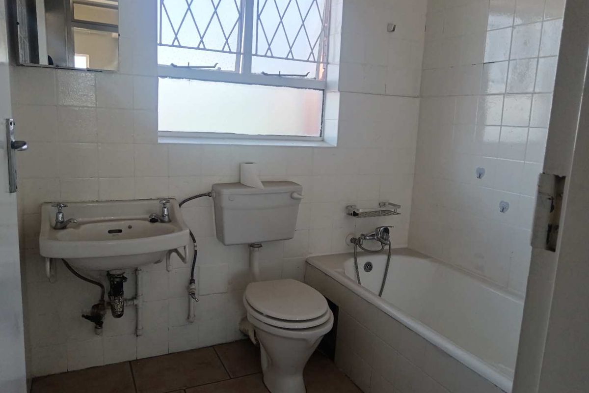 A dated bathroom featuring a wall-mounted basin, standard toilet, and bathtub with handheld shower mixer, finished with tiled walls and flooring.