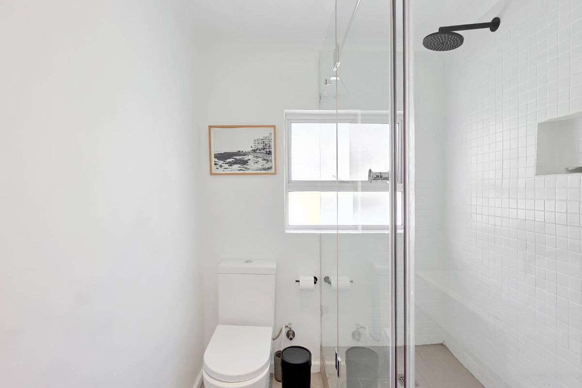 A clean, modern bathroom featuring a glass-enclosed shower with a rain shower head, white tiled walls, and a standard toilet.
