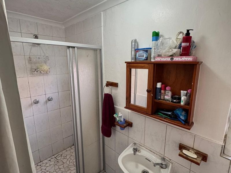 Compact bathroom featuring a shower enclosure with tiled flooring and a wall-mounted basin, requiring cosmetic updates to modernize the space.