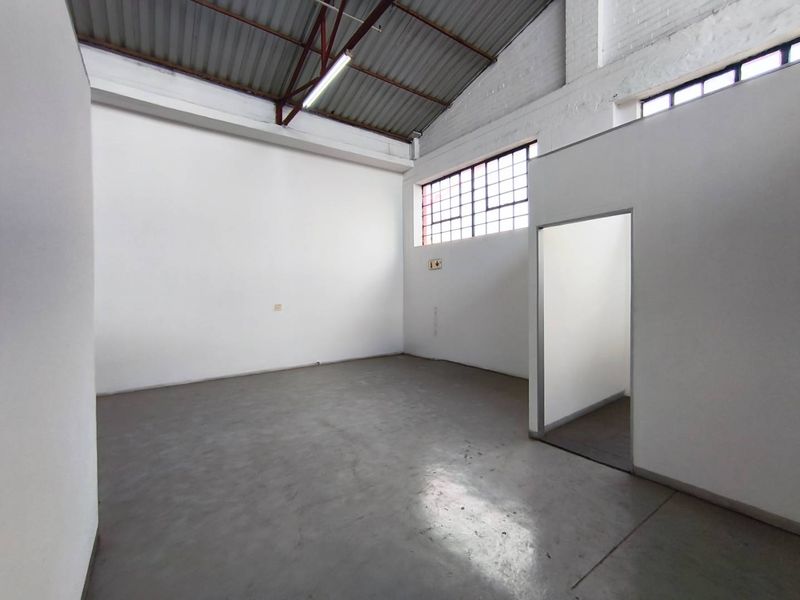 A clean, open-plan industrial utility space featuring high ceilings with exposed steel trusses, concrete flooring, and large steel-framed windows providing natural light.