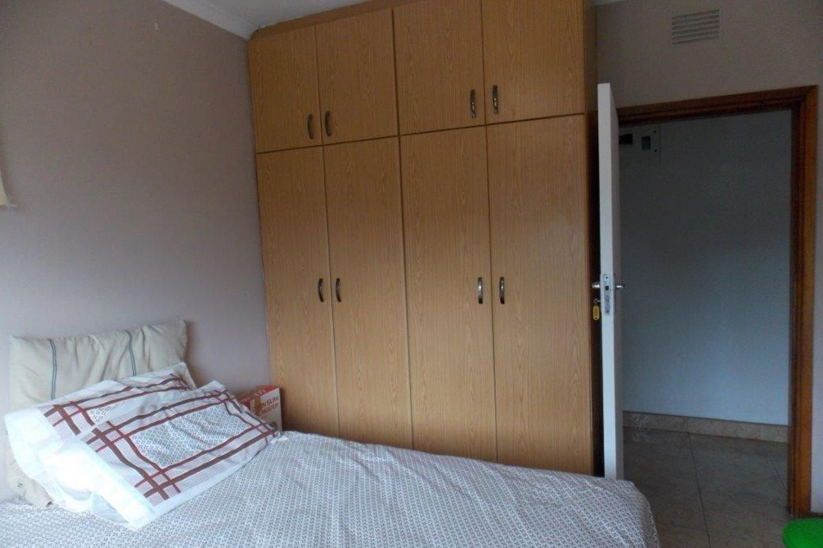 A bedroom featuring built-in wooden cupboards and tiled flooring, providing functional storage space within the room.