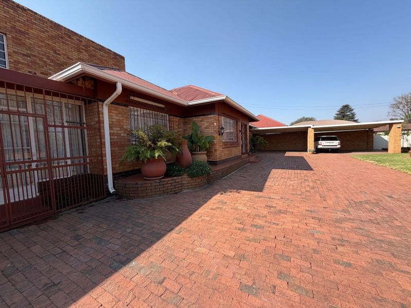 Front exterior view of a brick house featuring a spacious paved driveway, secure entrance gate, and a covered carport area.